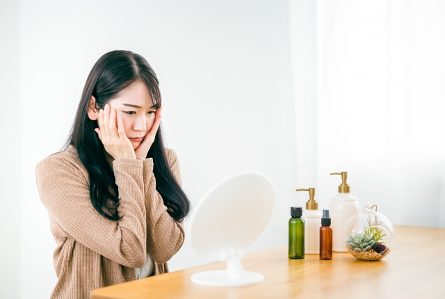 鏡をみながら両頬に手を当てる女性 