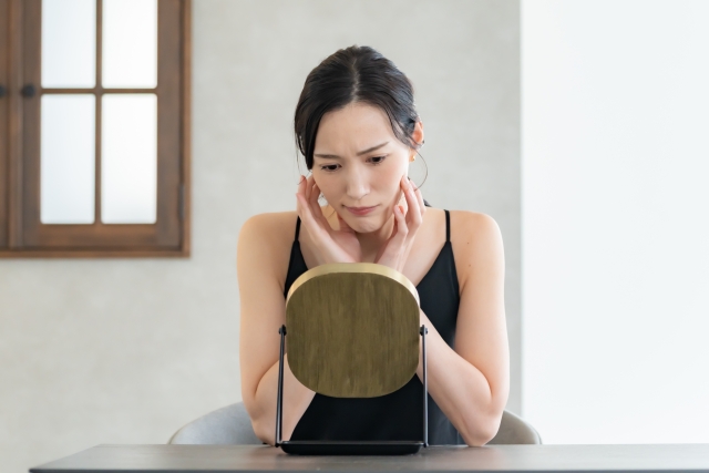 鏡を見てシミを気にする女性
